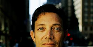 jordan belfort looks directly at the camera with a neutral expression on his face, he wears a white collared shirt that is unbuttoned at the neck