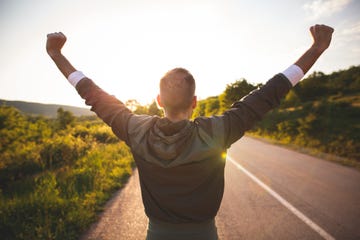 sport and life achievements and success concept sporty man raising arms towards beautiful sunset on the road