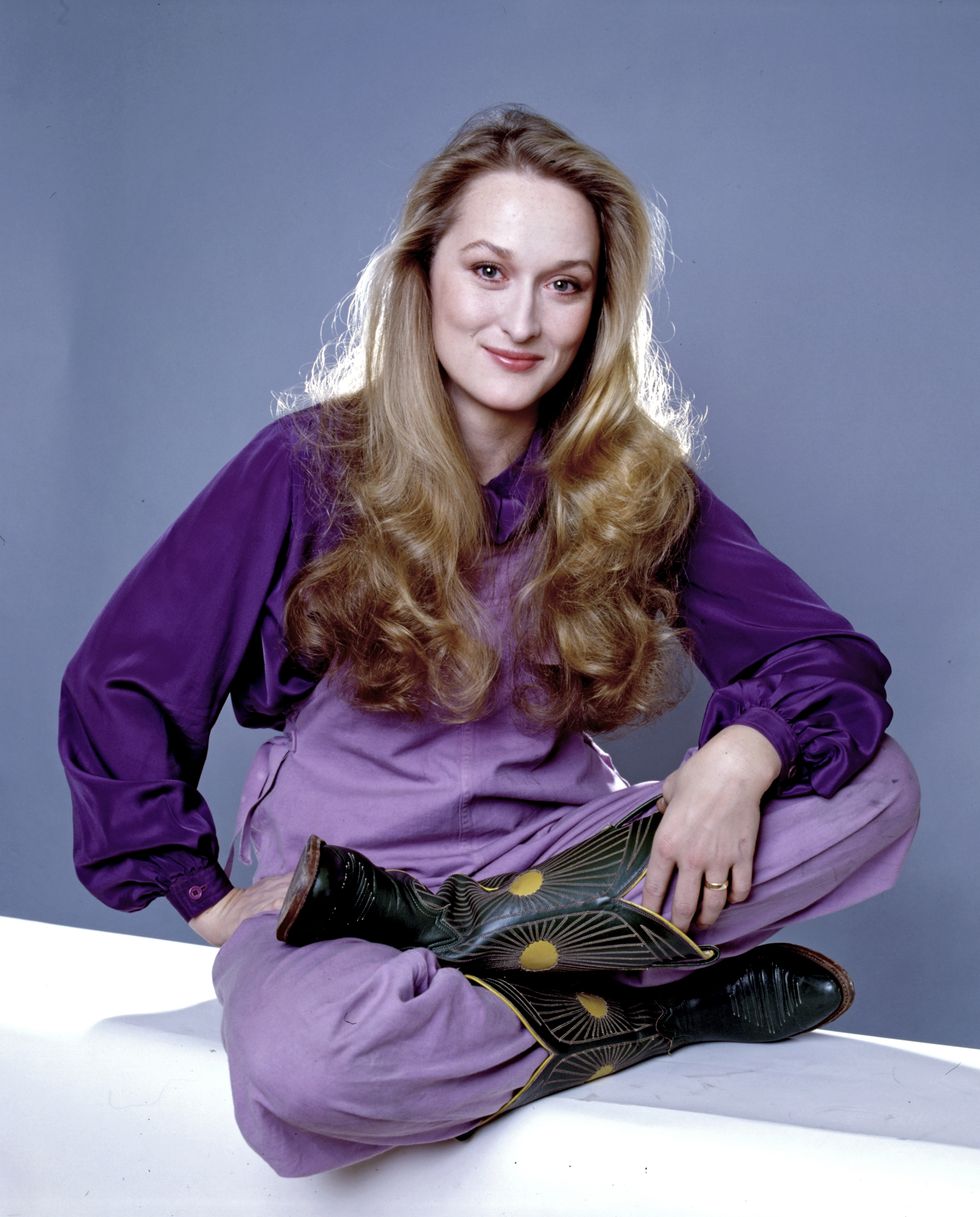 Meryl Streep sentada con mono morado y botas de cowboy