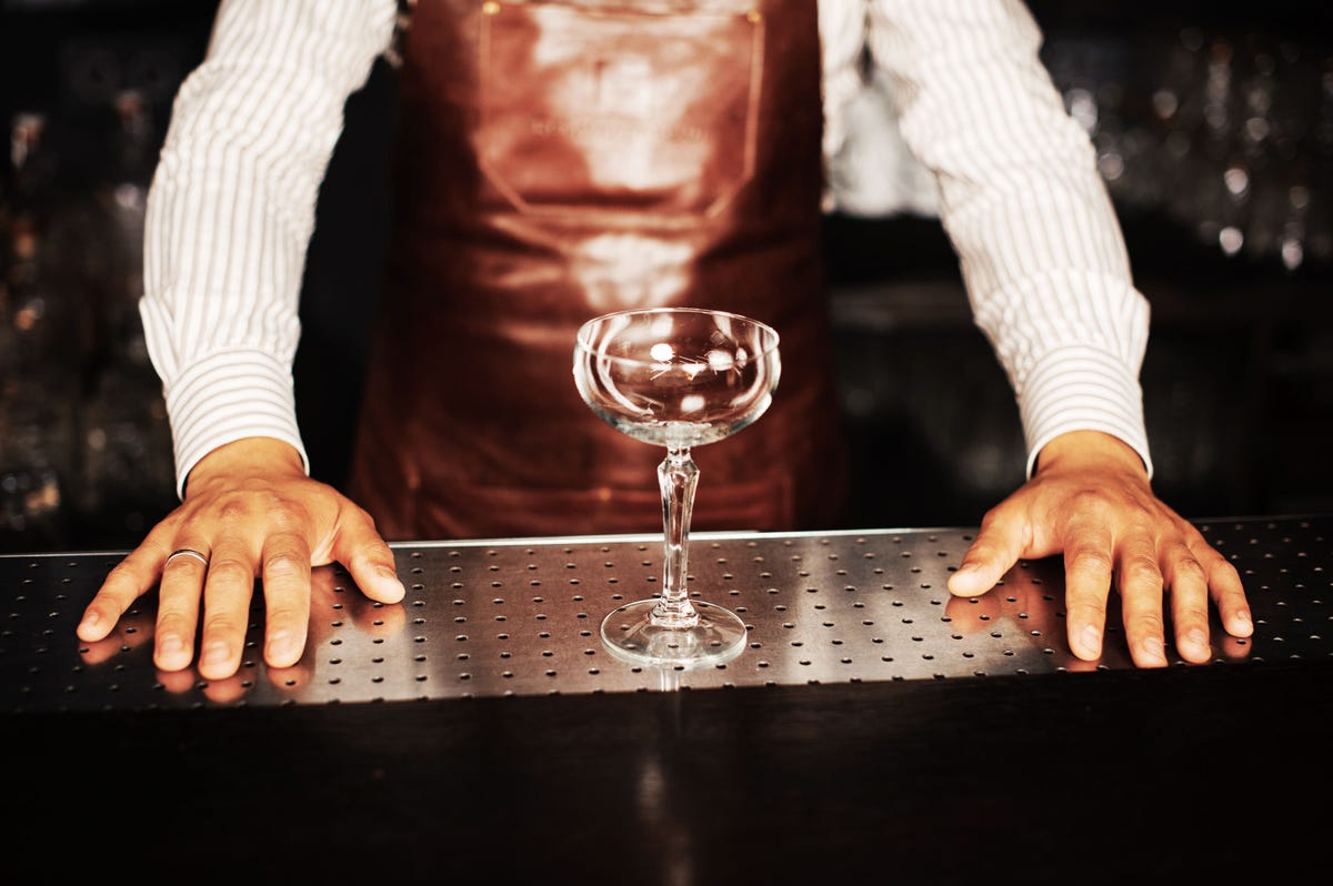 Wineglass stands on bar and woman bartender holds mixing cup and