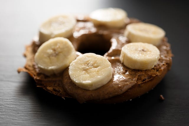 toasted bagel with almond butter spread and sliced banana, backlit with window light on a painted black chalkboard backdrop