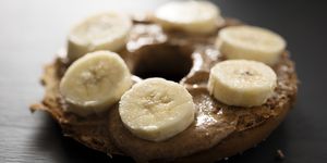 toasted bagel with almond butter spread and sliced banana, backlit with window light on a painted black chalkboard backdrop