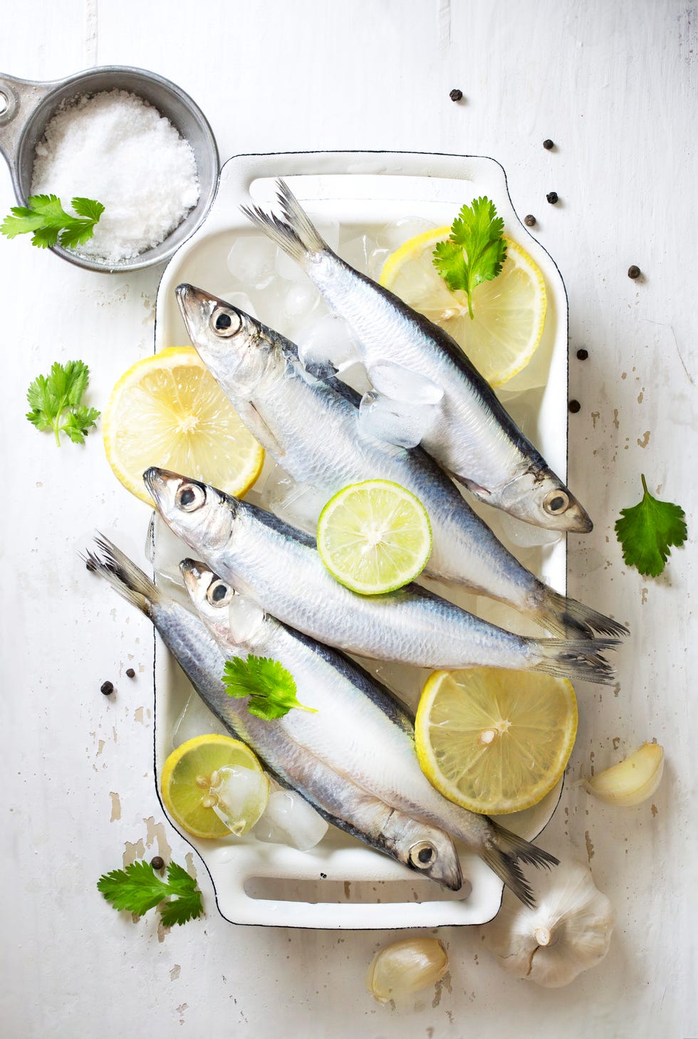 Chilled fresh uncooked sardines with herbs and lemon slice on white background.