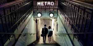 Couple of young people entering a station of the Paris Metro at night. Paris, France
