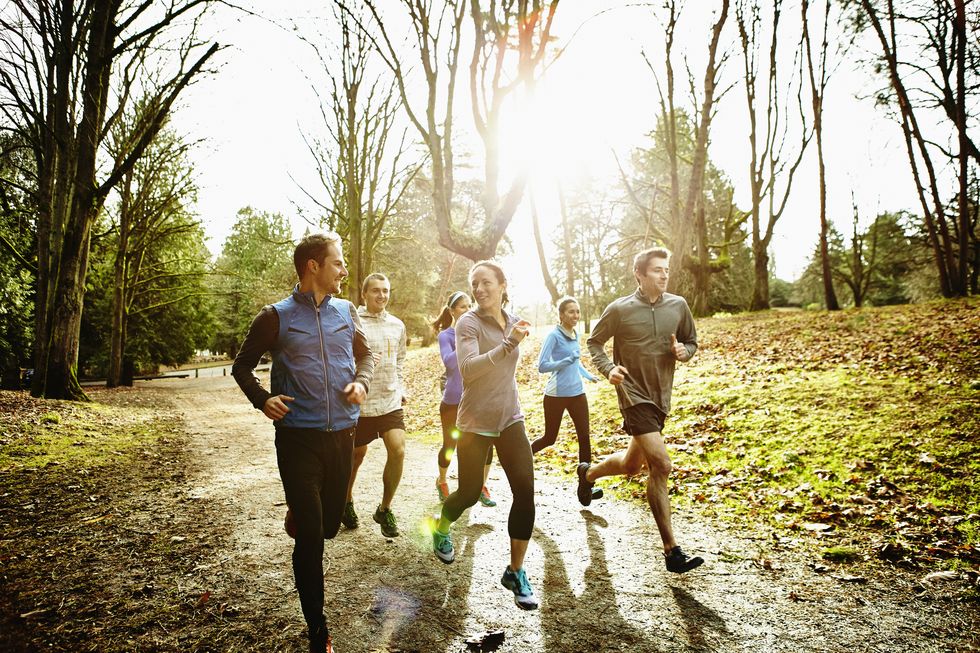 smiling group of male and female runners trail running together in park