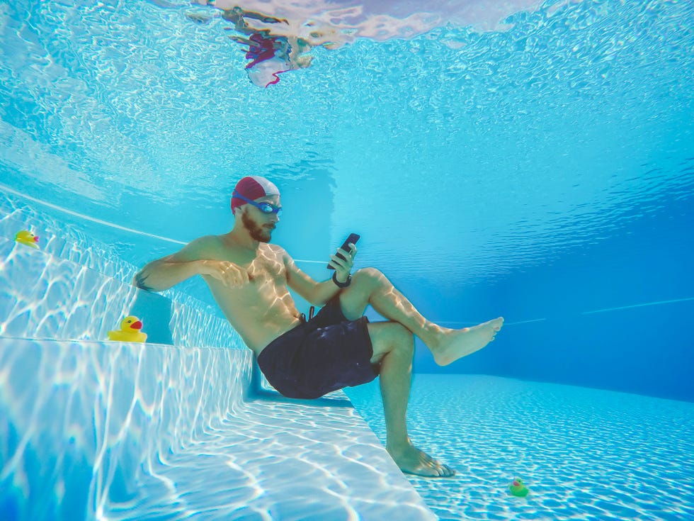 workaholic man underwater, social networking on the mobile phone he is surrounded by small yellow plastic ducks