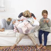 Exhausted mother with laundry basket on couch with children using digital tablet and cell phone
