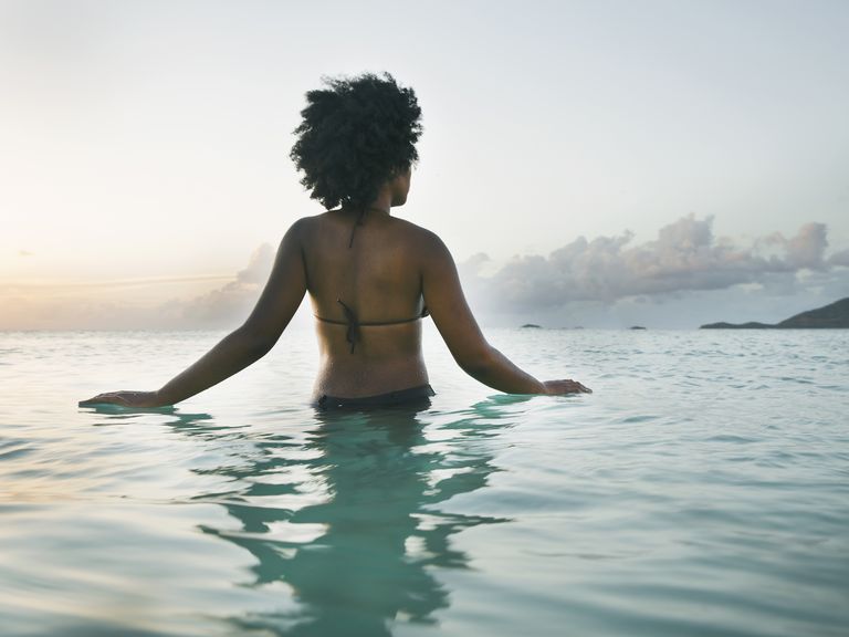 Young black woman wading into ocean, rear view.