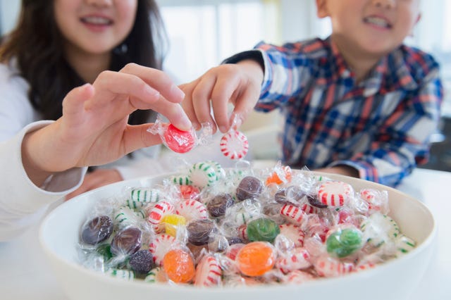 hands reaching for colorful candies from a large bowl