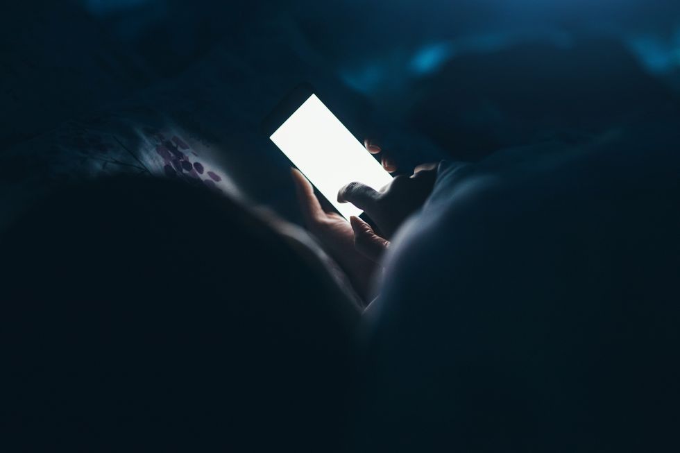 woman texting and reading on smartphone in bed in midnight