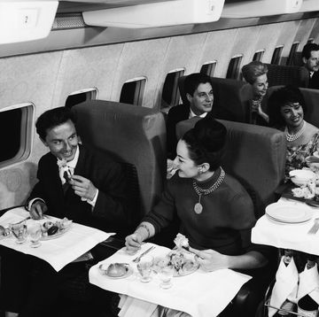 interior view of the first class compartment of a commercial passenger plane a boing shows, in the foreground, a well dressed couple as they smile and enjoy their meal, while behind them a flight attendant in a bow tie serves another happy couple, 1950s photo by authenticated newsgetty images