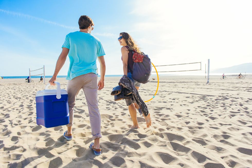Young couple walking on beach, holding cool box, rear view