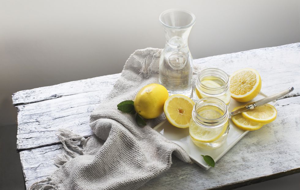 fresh lemon and glasses of lemon water on white rustic  wooden table top vintage style still life food styling shot