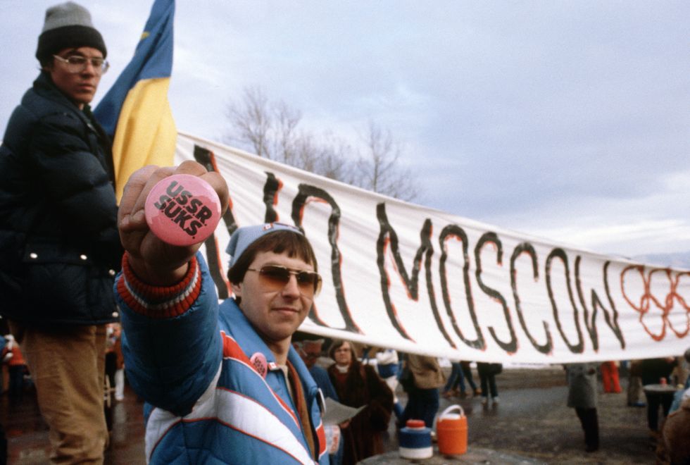 american protesters at the lake placid games opening ceremony hold various signs of protest against the russians including a sign fostering boycott of the 1980 moscow summer olympic games