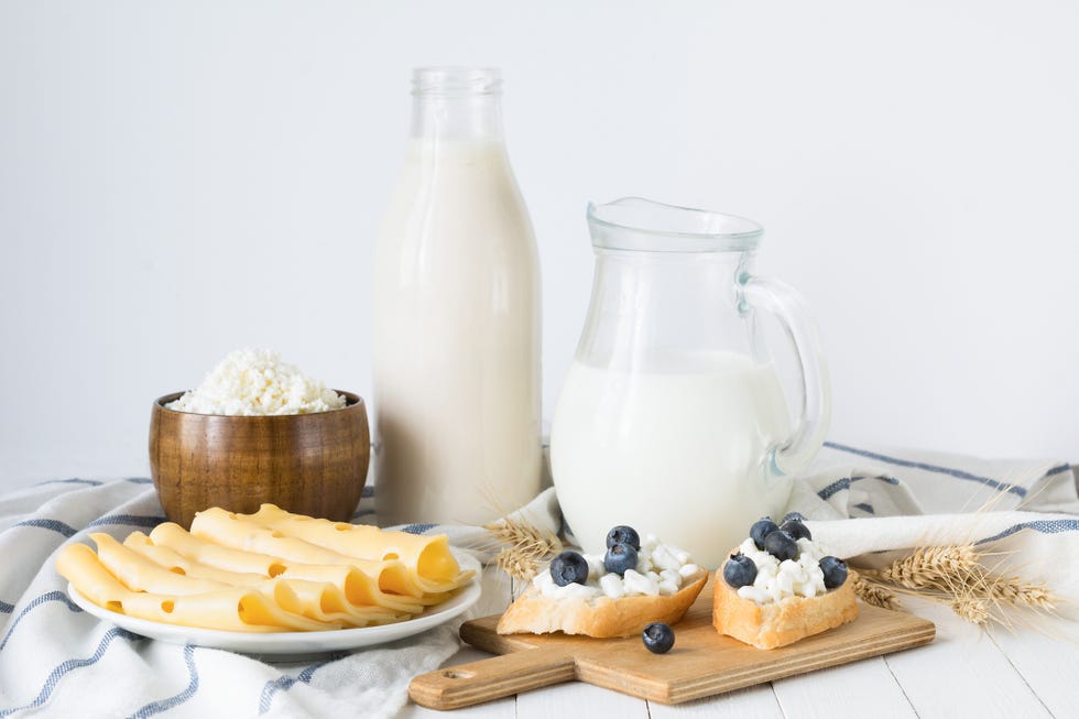 bottle of baked milk, curd, farmers cheese, sliced yellow cheese and toasts with blueberries on wooden chopping board