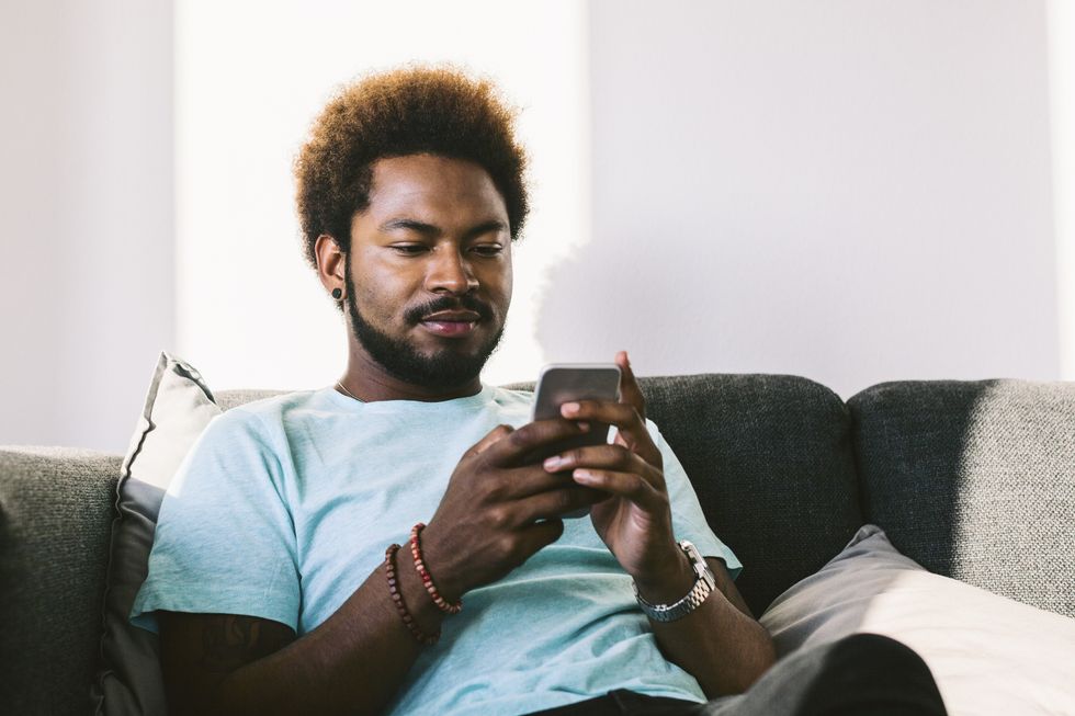 Young man at home reading messages on smart phone