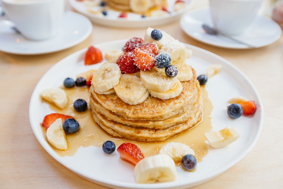 stack of pancakes with maple syrup, banana, strawberry and blueberry on the plate