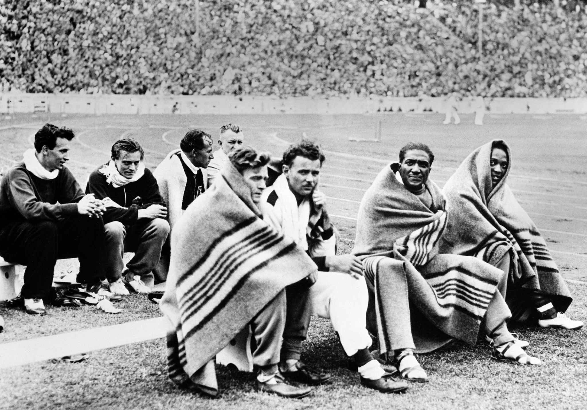 here are some of the contestants in the 100 meters dash at the olympic games in berlin, swathed in blankets after running their race  left to right, are frank wykoff, us, who finished fourth haenny, switzerland ralph metcalfe, of the united states and jesse owens, united states, who won the event