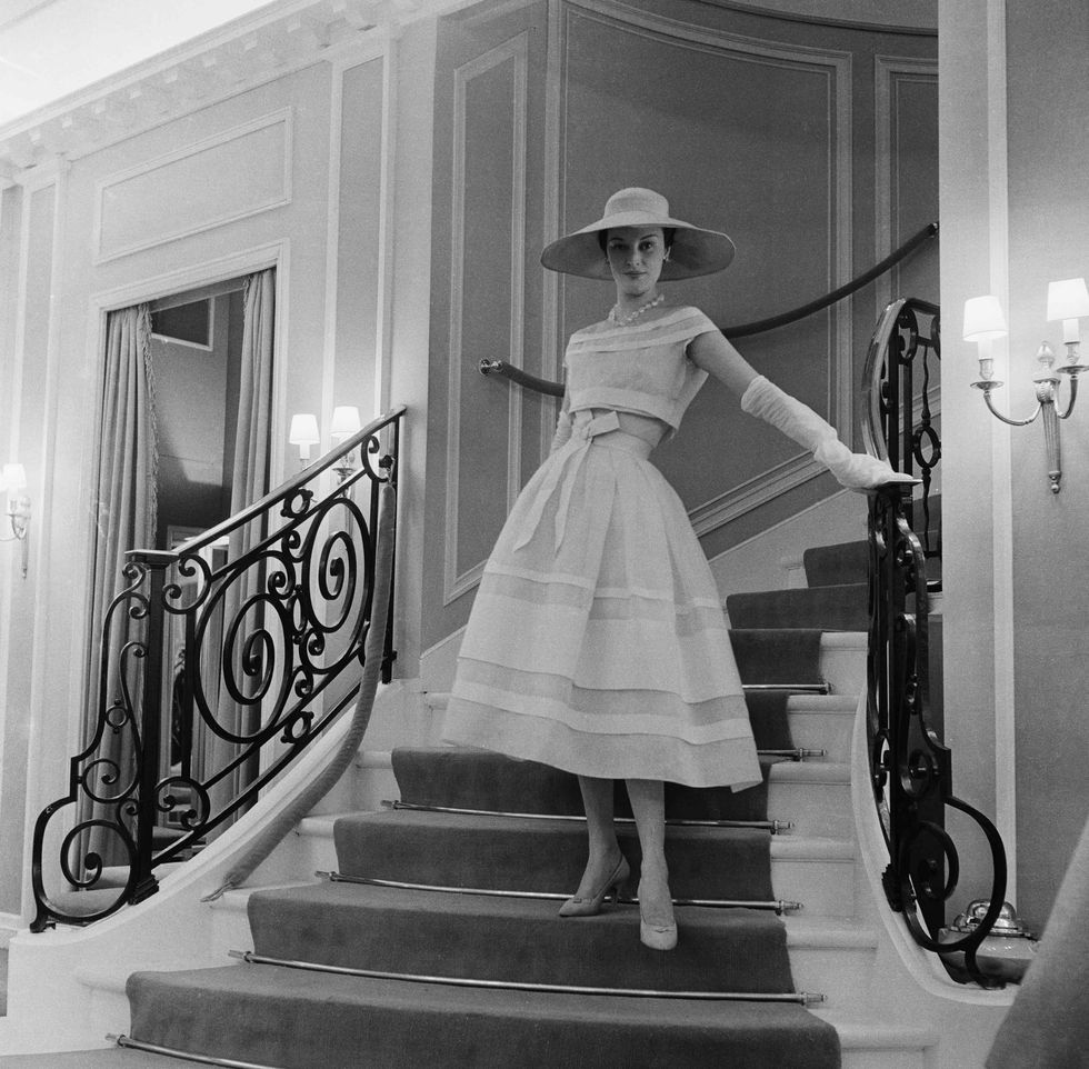 a model wearing a dior dress, posing on the stairs of 30 montaigne in 1956