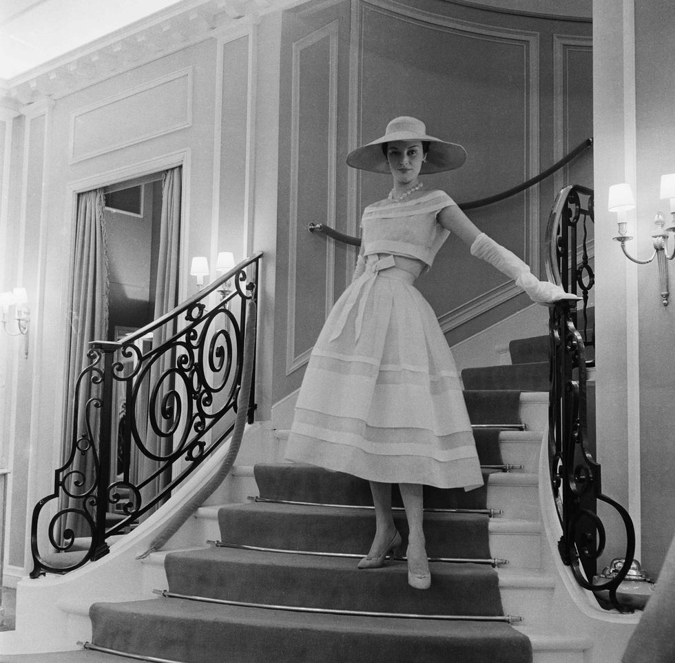 a model wearing a dior dress, posing on the stairs of 30 montaigne in 1956