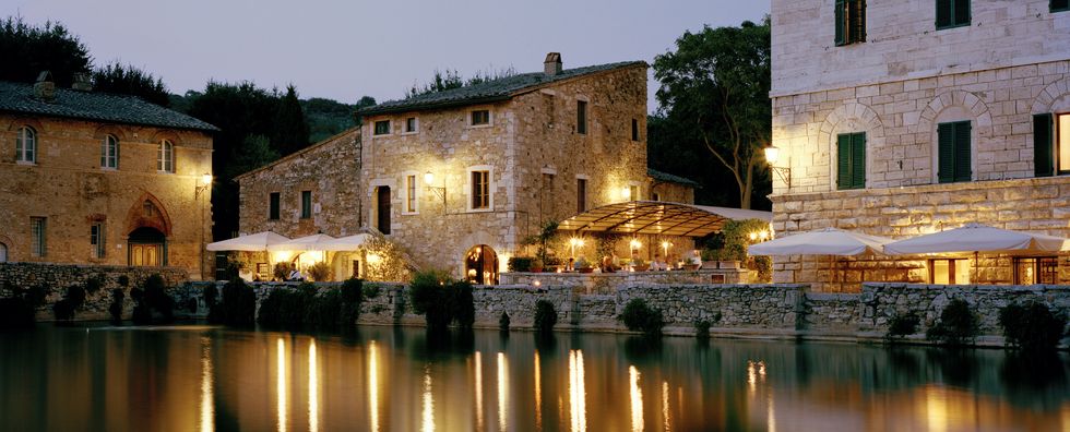 italy, tuscany, bagno vignoni, people dining by ancient thermal bath at dusk