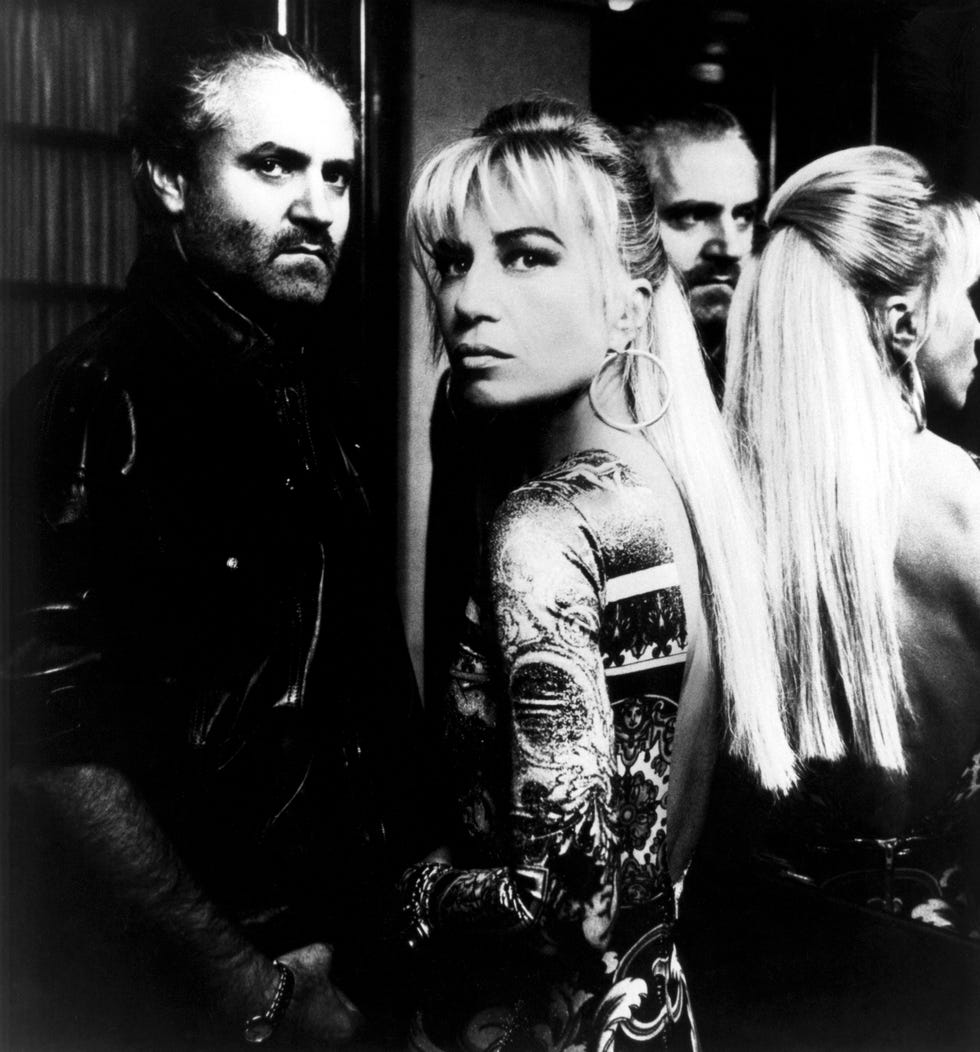 gianni versace and donatella versace stand facing each other but look to the camera