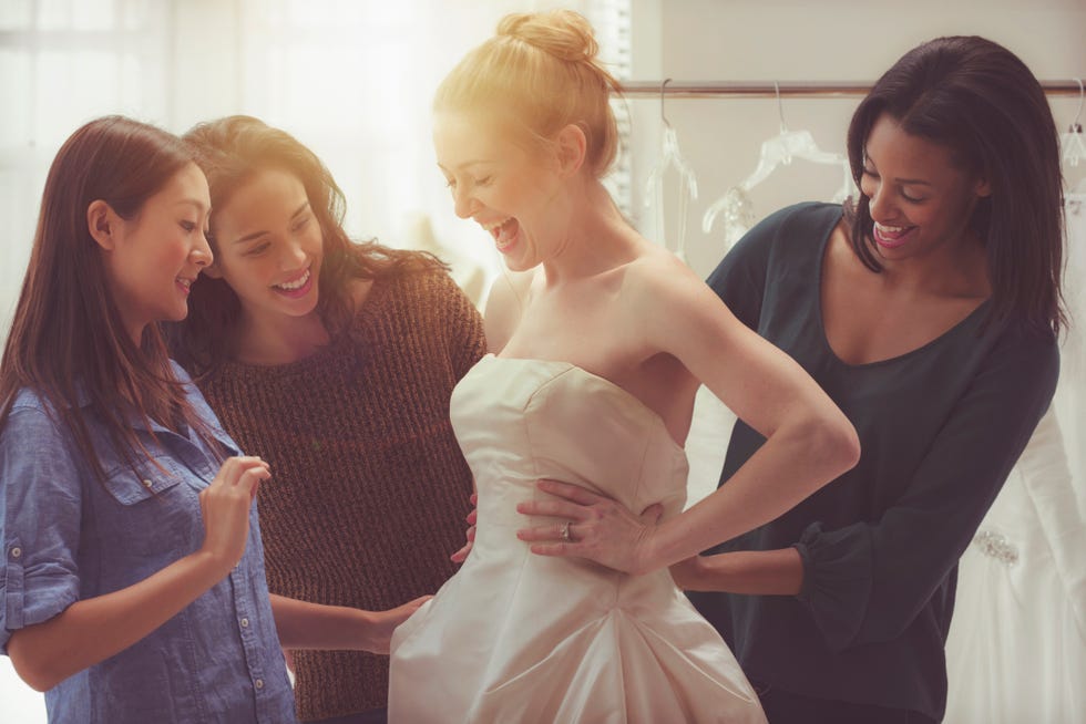 bride trying on wedding dress with three friends