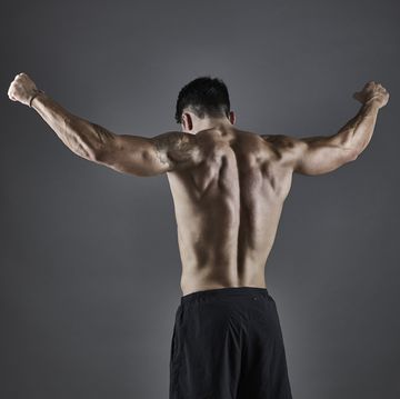 young athletic male bodybuilder standing with arms raised, showing strength of back and arm muscles