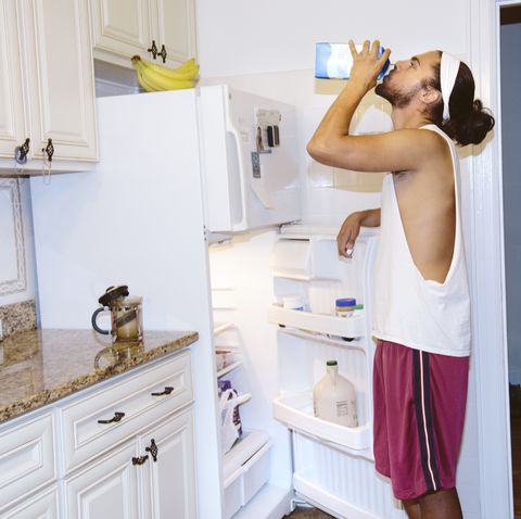 young man standing next to open fridge, drinking milk from carton