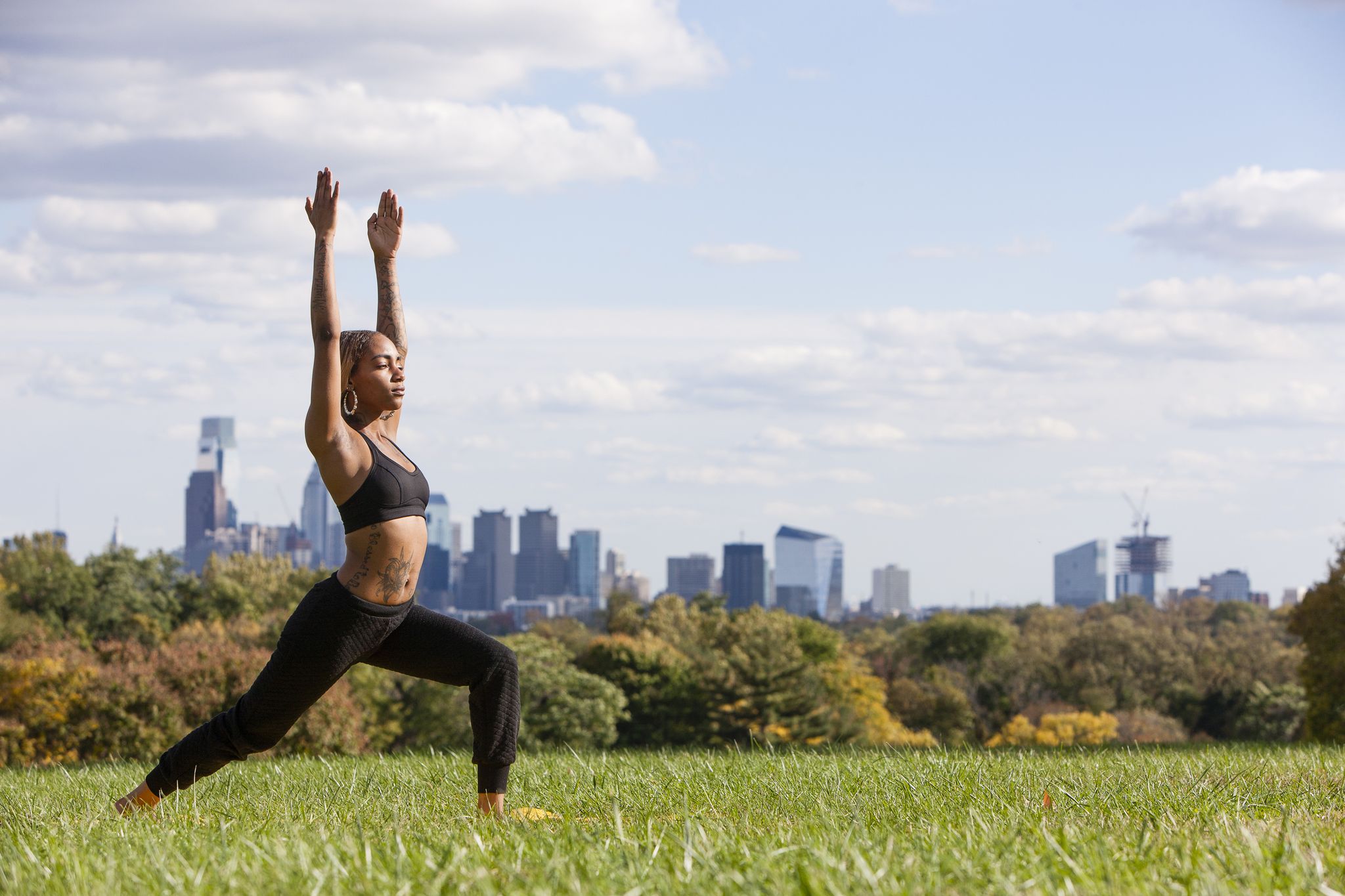 Side view of young woman on grass in yoga position, arms raised, eyes closed, Philadelphia, Pennsylvania, USA