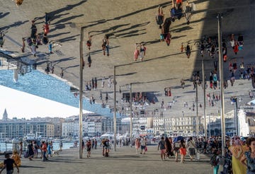 people reflecting themselves on a giant mirror roof on a street near the port of marseille