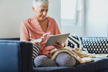 a person sitting on a couch with a tablet and a blanket