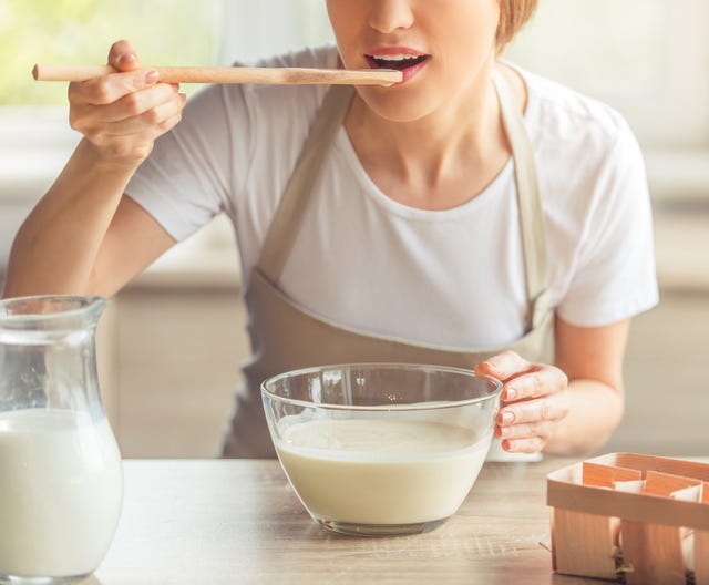 cropped image of beautiful woman in apron tasting liquid dough for baking muffins