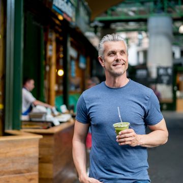 healthy man drinking a smoothie and walking on the street looking happy