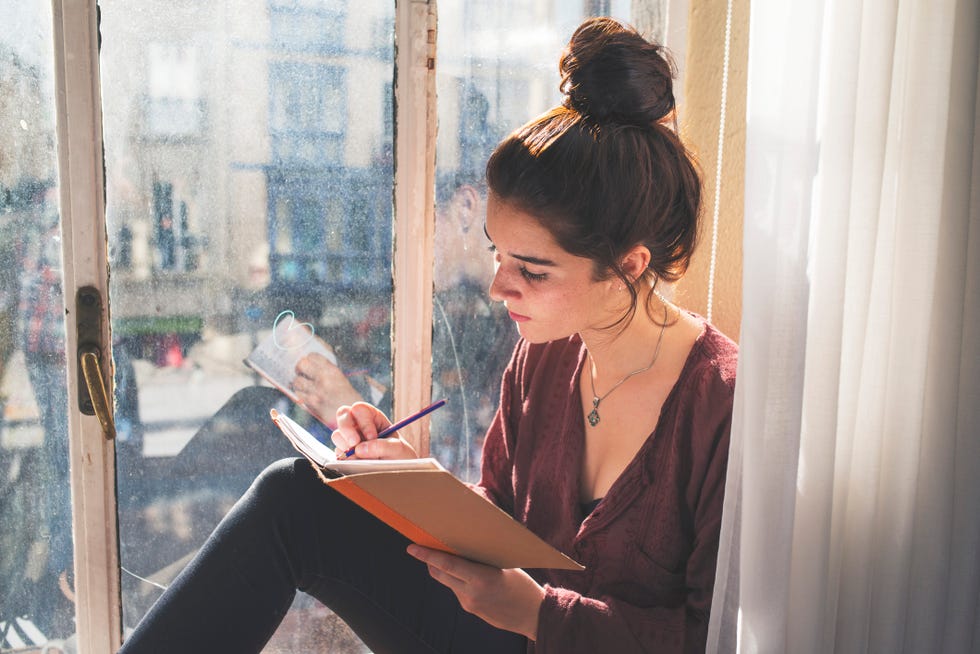 young woman writes daily next to the window