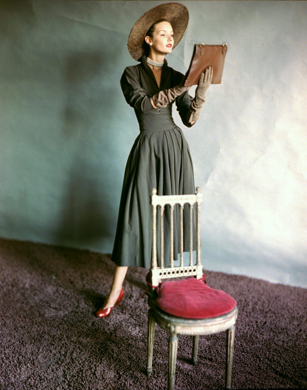 model standing behind chair wearing a small jacket and pleated skirt with cummerbund by claire mccardell with straw hat by brewster and envelope bag by phelps. (photo by horst p. horst/condé nast via getty images)