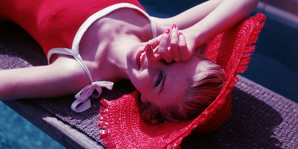 a young woman, wearing a red swimsuit and sunhat, shades her eyes from the sun as she relaxes above the crystalline waters of a swimming pool ca 1955 photo by © hulton deutsch collectioncorbiscorbis via getty images