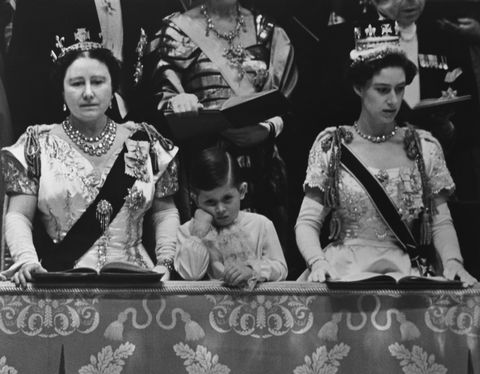 elizabeth the queen mother, prince charles, and princess margaret watch queen elizabeth ii’s coronation, the two women are wearing ornate gowns, sashes, crowns and jewelry, charles is wearing a fancy long sleeve shirt