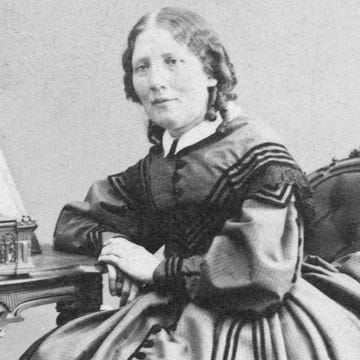 harriet beecher stowe sits for a photography while leaning against a desk, she wears a large long sleeve gown