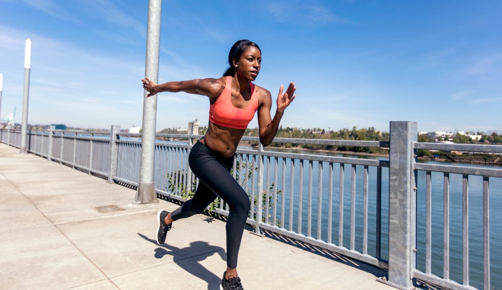 african american adult female sprinting next to a body of water in an urban environment