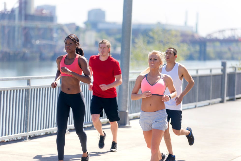 diverse group of young adults running together next to a body of water