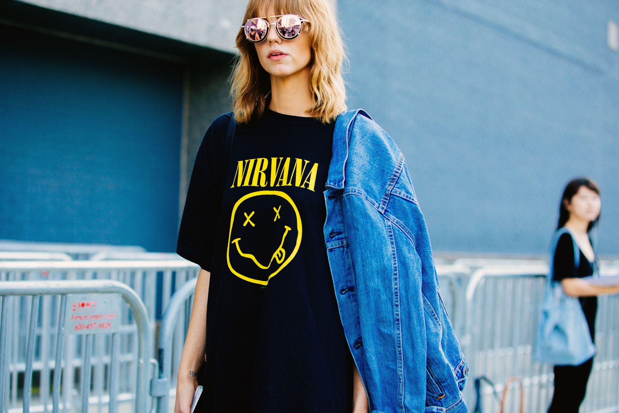 model michi delane wears vintage style reflective sunglasses, a black nirvana t shirt, and a denim jacket off her shoulder after the lacoste show at spring studios on september 10, 2016 in new york city