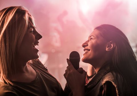 Two cheerful women singing karaoke at disco club.