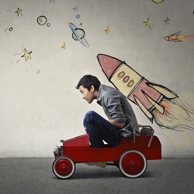 the portrait of a young asian guy in a red toy car in front of a gray wall with spaceship and planets