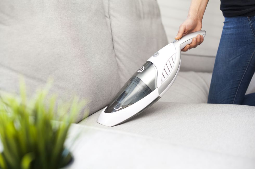 woman with handheld vacuum cleaning on sofa