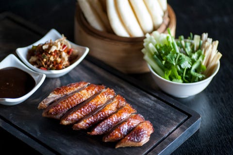 Chinese Style Sliced Duck Breast roasted sliced chinese style duck breast on a dark wooden chopping board with sweet soy dip and chopped chilli sauce, with asian greens and steamed rice buns on the side