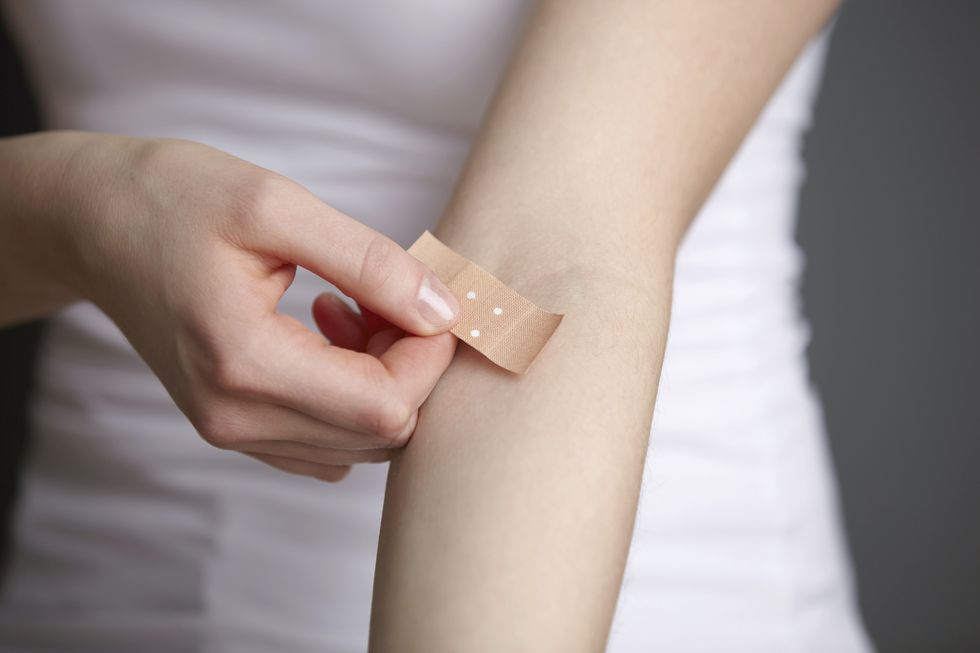 cropped close up shot of young woman applying adhesive plaster to her own arm