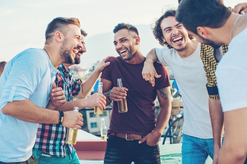 multi ethnic group of young men chatting and drinking beer on a rooftop party