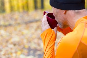 male runner drining from plastic thermos cup at autumn forest background