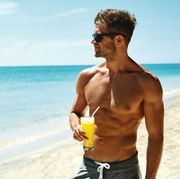 summer relax portrait of athletic sexy man with muscular body drinking fresh juice smoothie cocktail on tropical beach handsome fitness male model sunbathing, enjoying refreshing drink on vacation